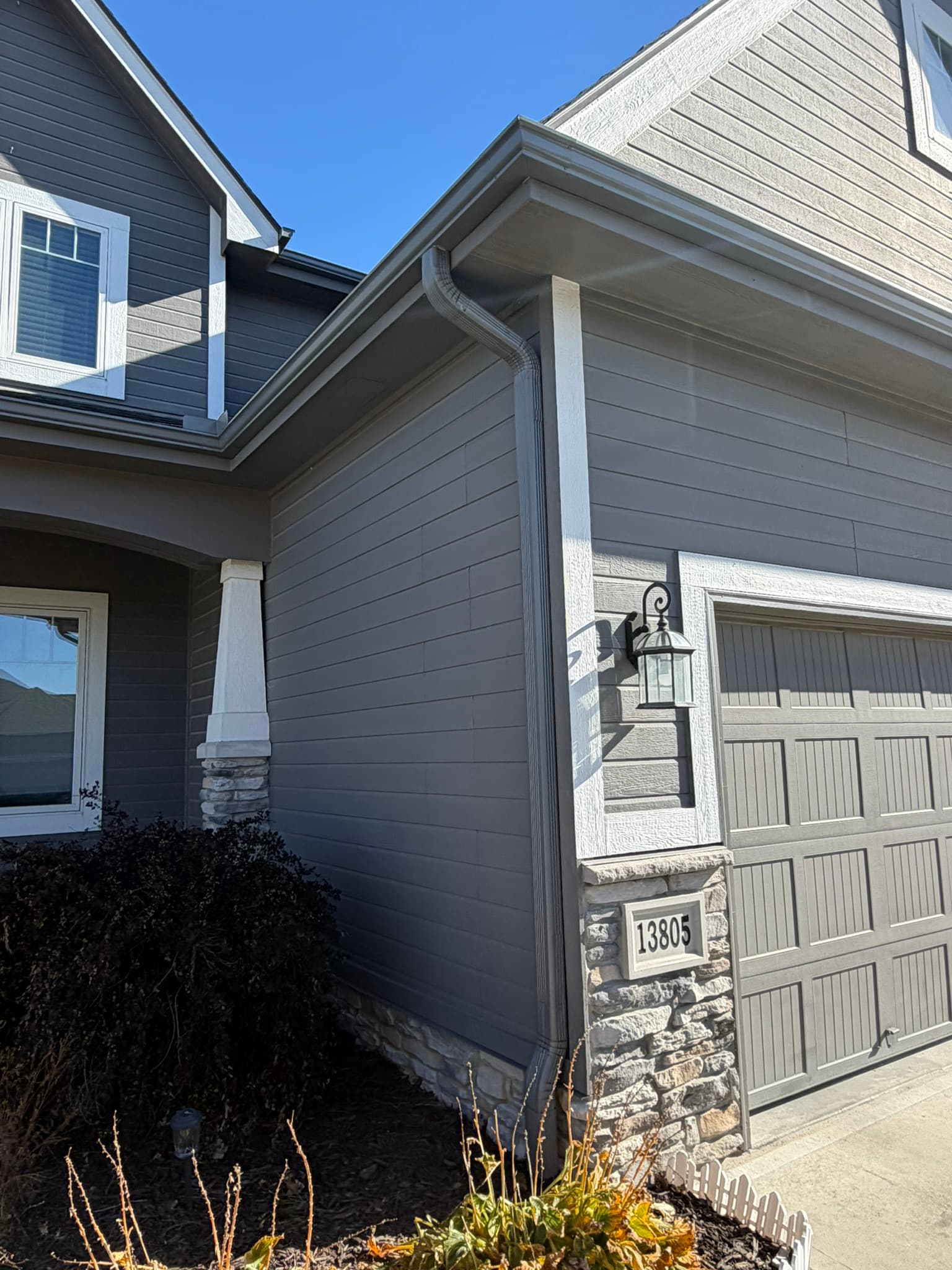 Gray seamless gutter and downspout along the lap siding of a home, inspected for hail dents