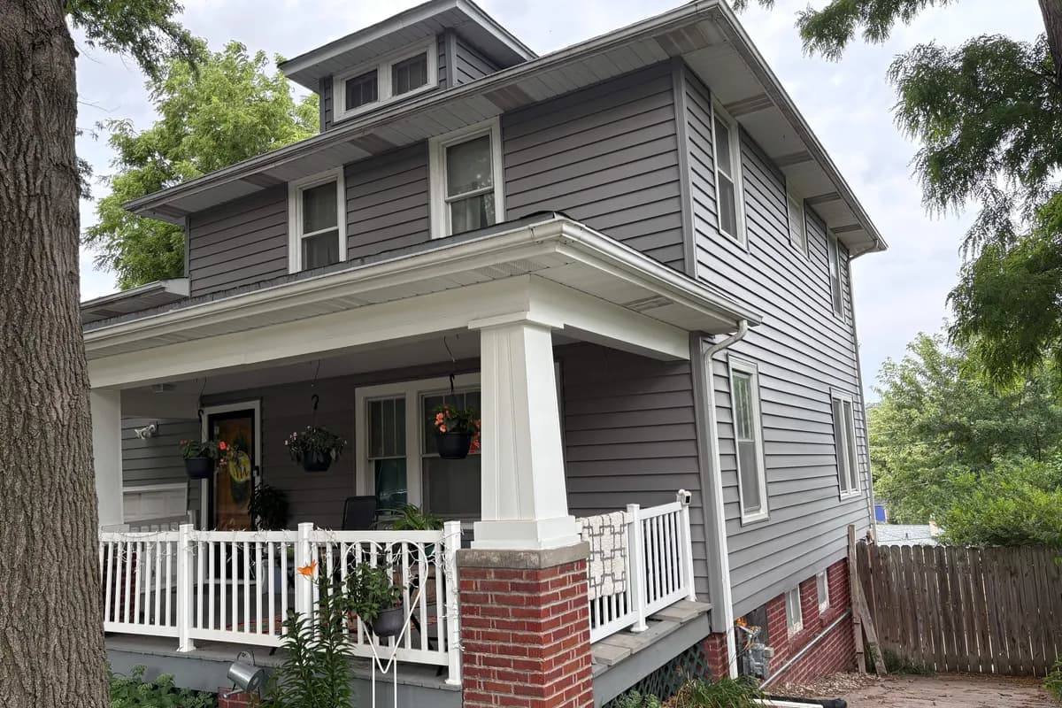 Field Club foursquare home with a hipped dormer roof, gray siding, and a white wraparound porch on brick piers