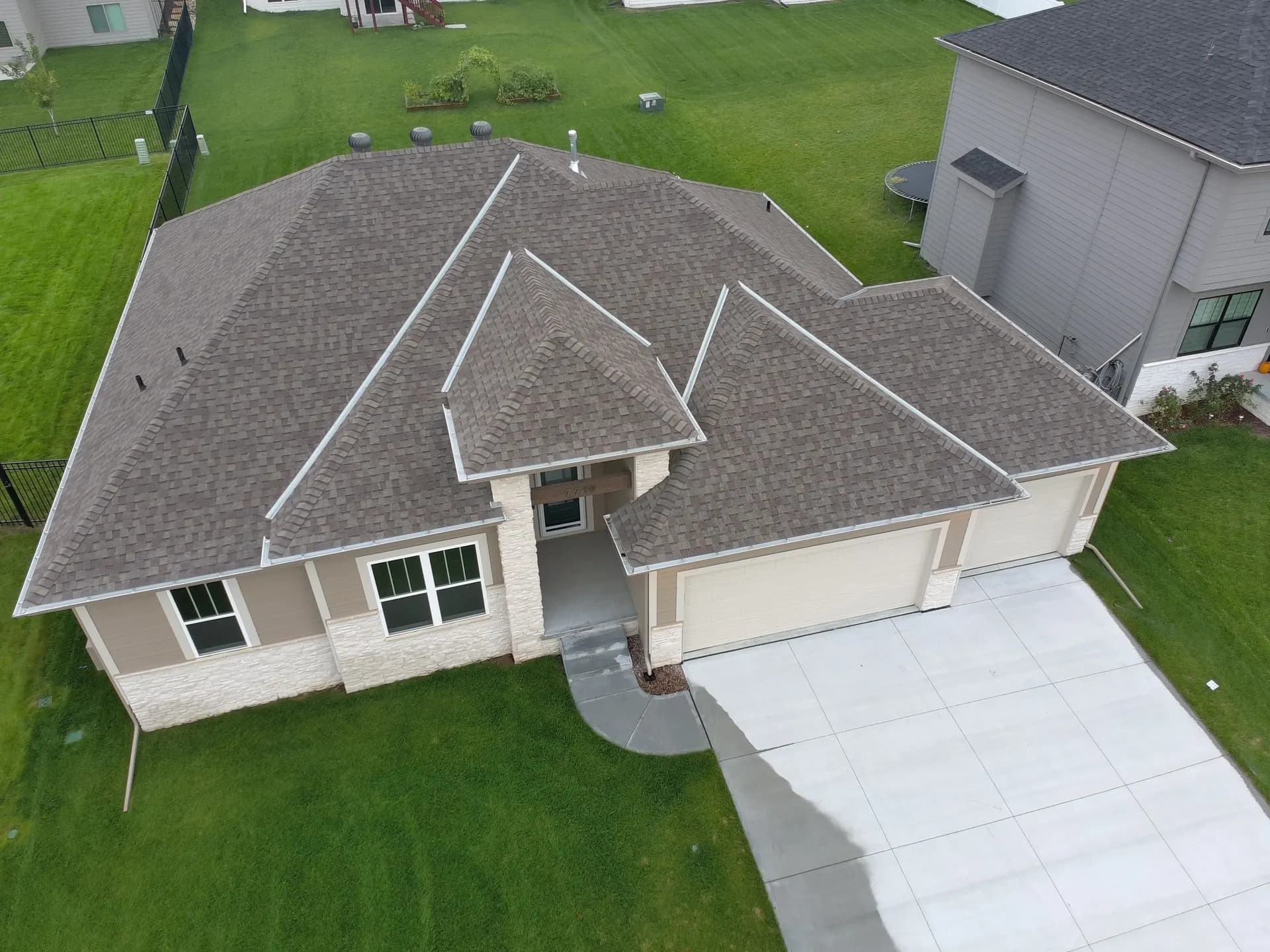 Aerial view of a new ranch home with a brown architectural shingle hip roof and three-car garage in Gretna, Nebraska