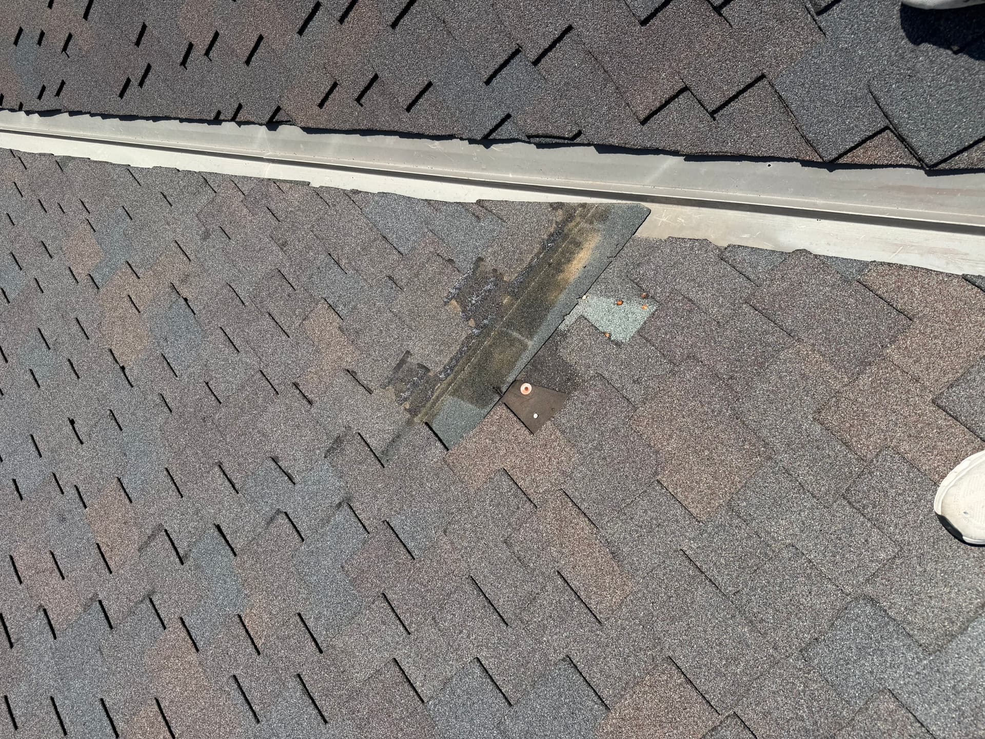 Missing shingle tabs exposing the underlayment next to a metal valley on a Papillion roof