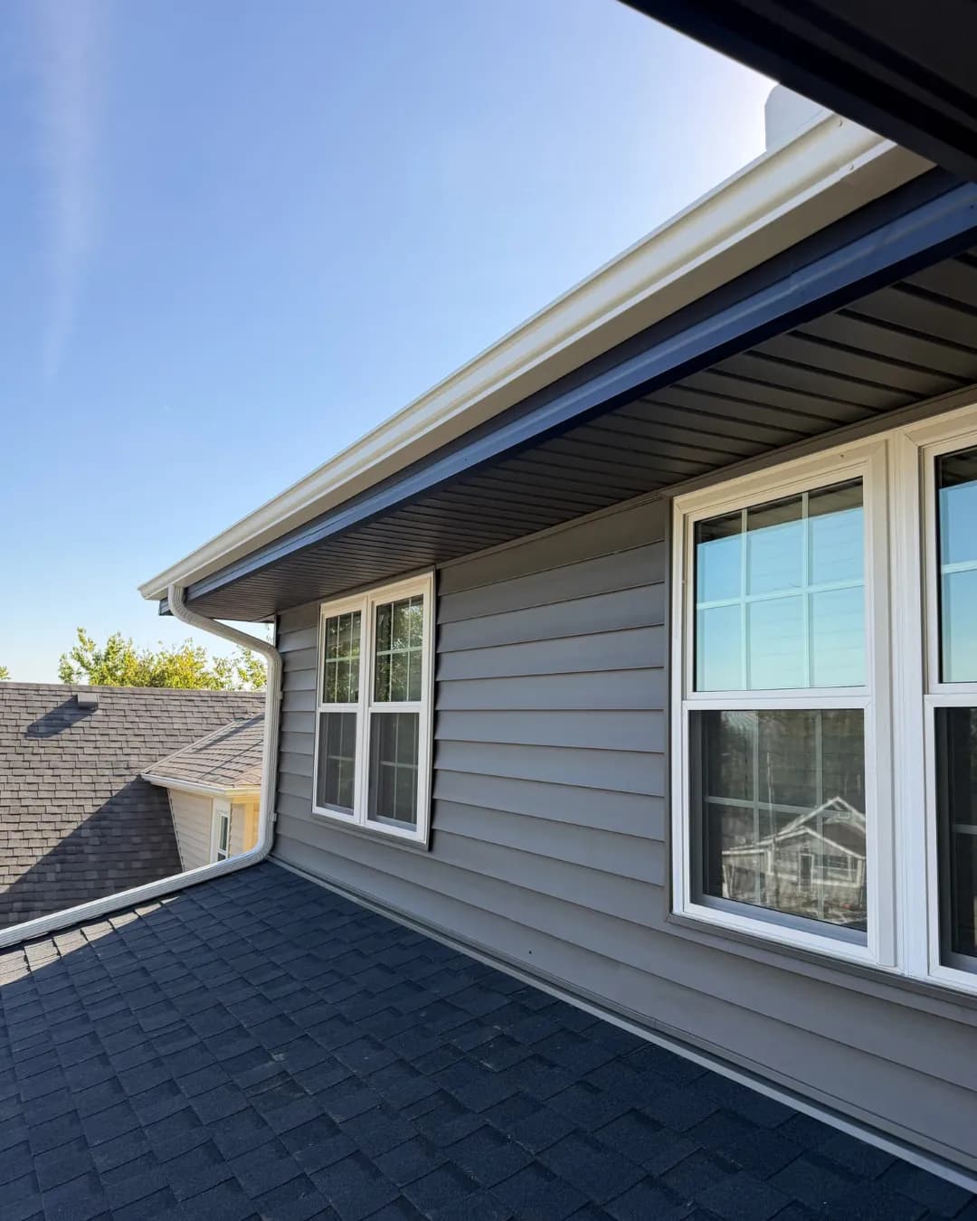 Clean gutter, downspout, and dark shingle roofline beside gray siding on an Omaha home