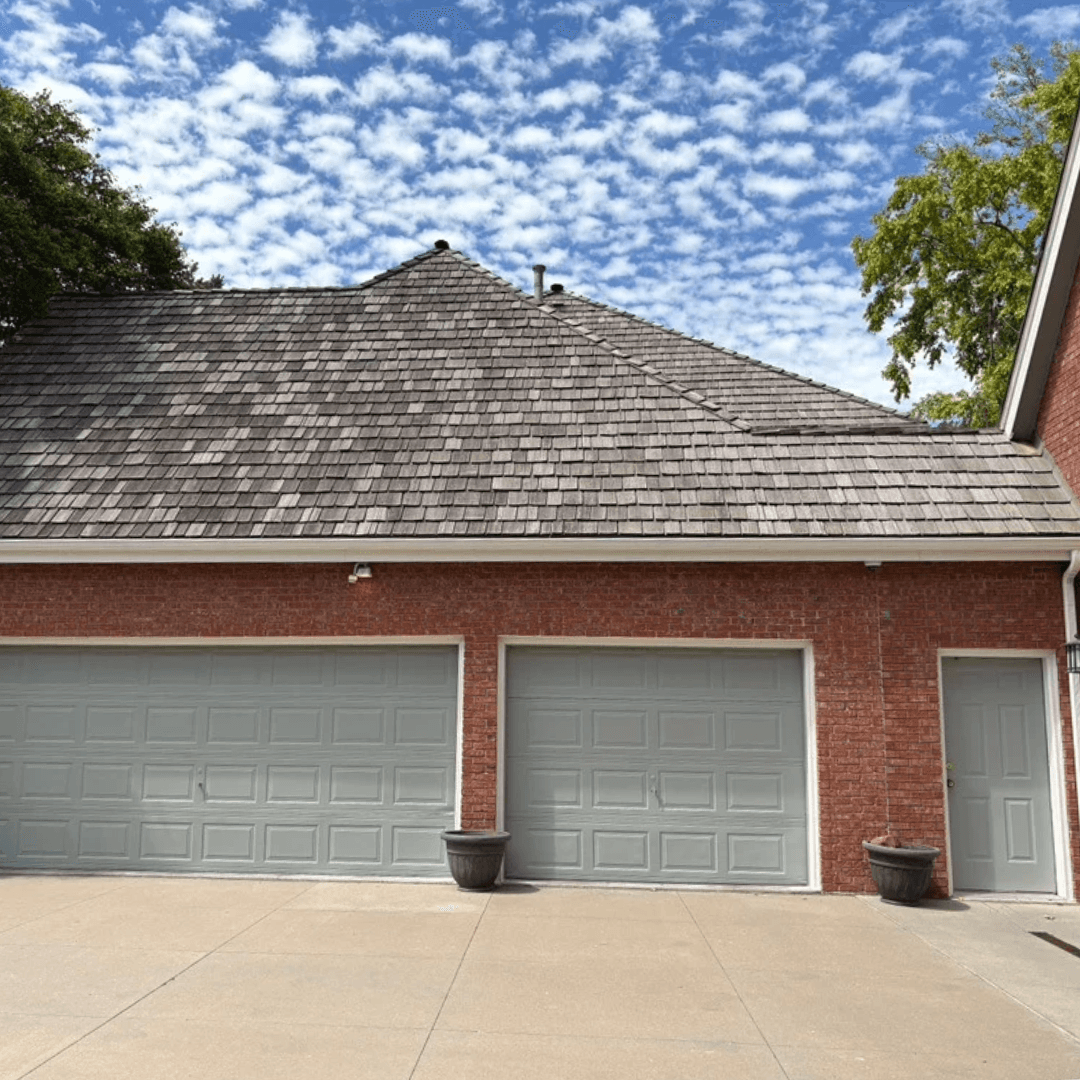 Weathered gray cedar shake hip roof over a red brick three-car garage in Omaha
