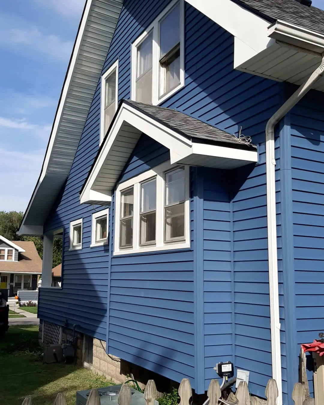 Blue vinyl lap siding with white trim and a shingled window bump-out on a Field Club bungalow