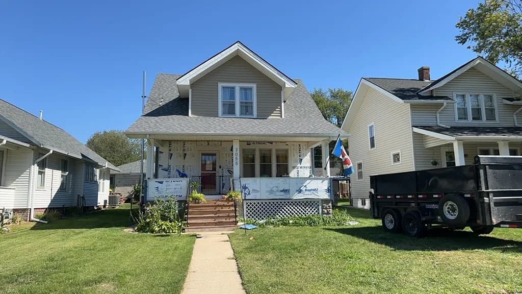 Older Omaha home wrapped in house wrap mid siding replacement, with a Royalty dump trailer parked out front