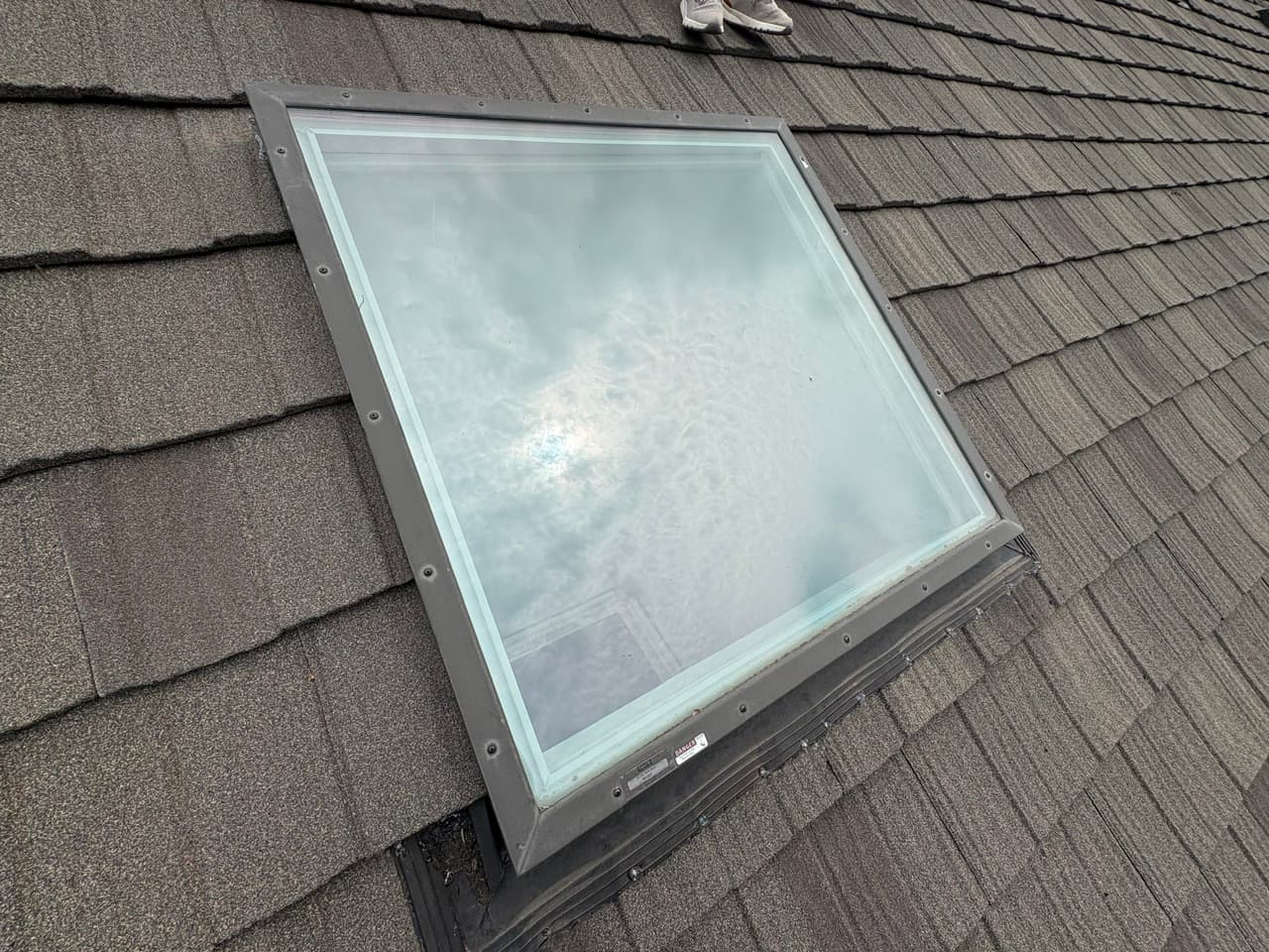 Skylight on an Omaha shingle roof with improper flashing sealed by exposed membrane and caulk instead of manufacturer step flashing